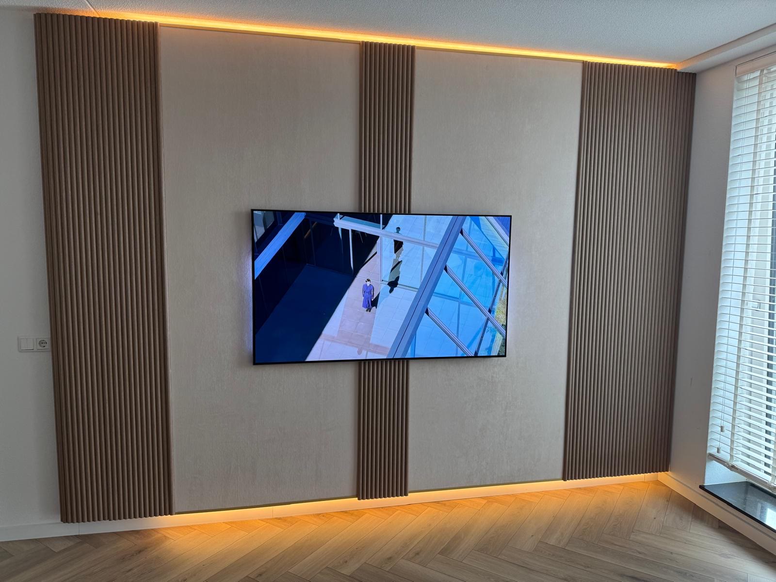 Na: Dezelfde wand afgewerkt met houten lattenpanelen en lichte wandpanelen, met warme indirecte verlichting