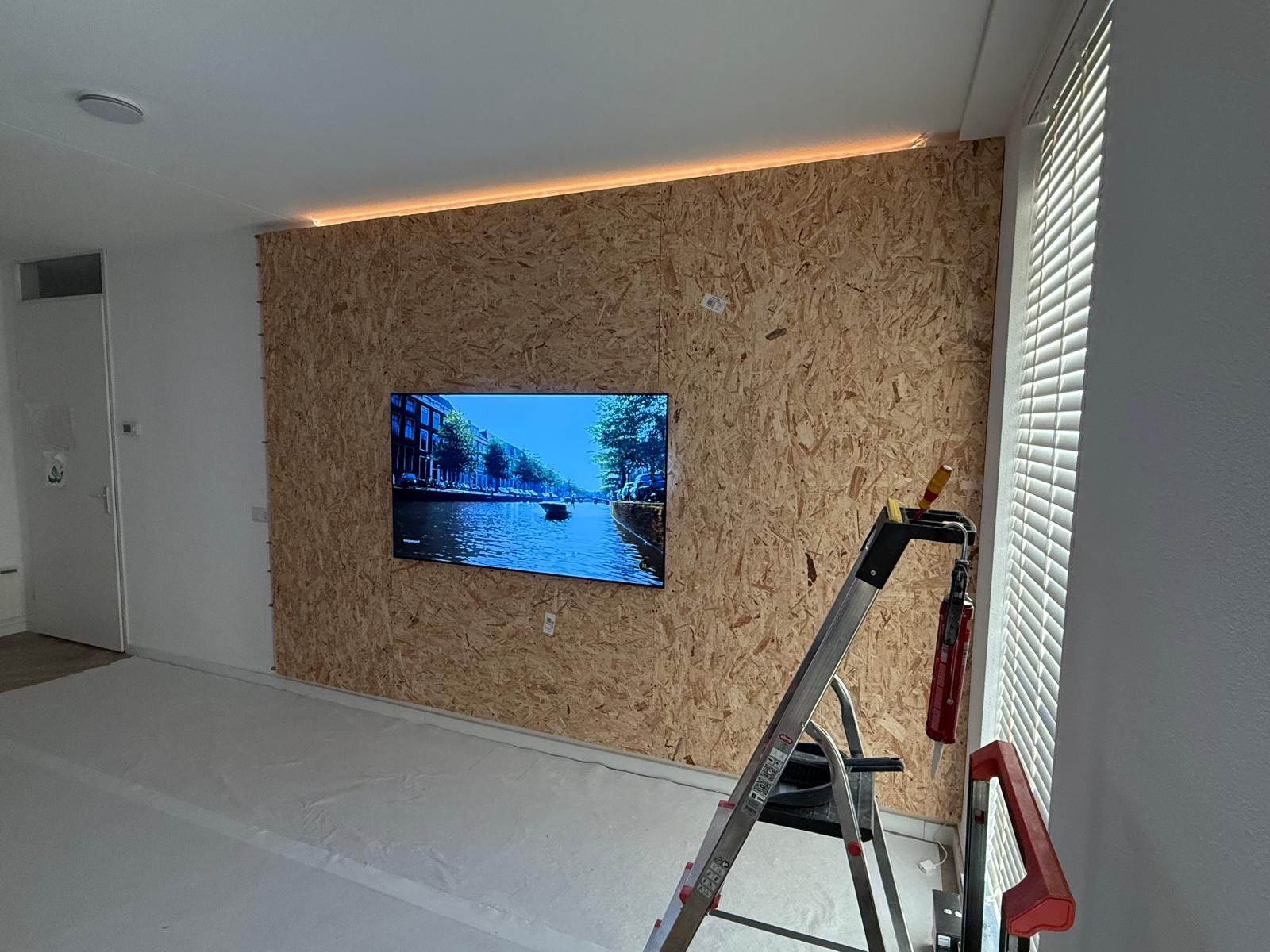 Wand bekleed met plaatmateriaal, de televisie teruggehangen en de indirecte verlichting bovenlangs aan