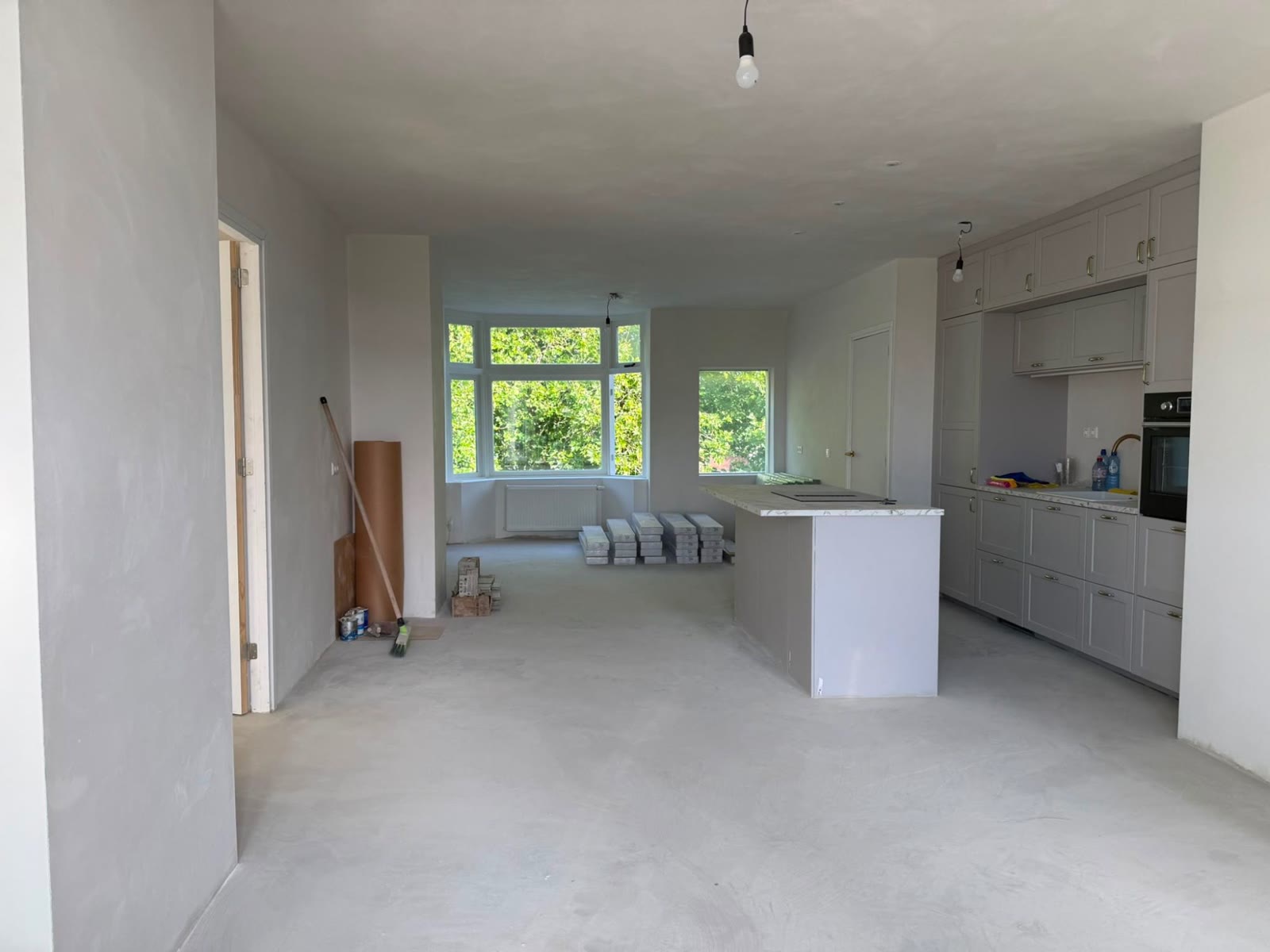 Na: Dezelfde ruimte gestuct, met een gestorte dekvloer en een geplaatste keuken met kookeiland