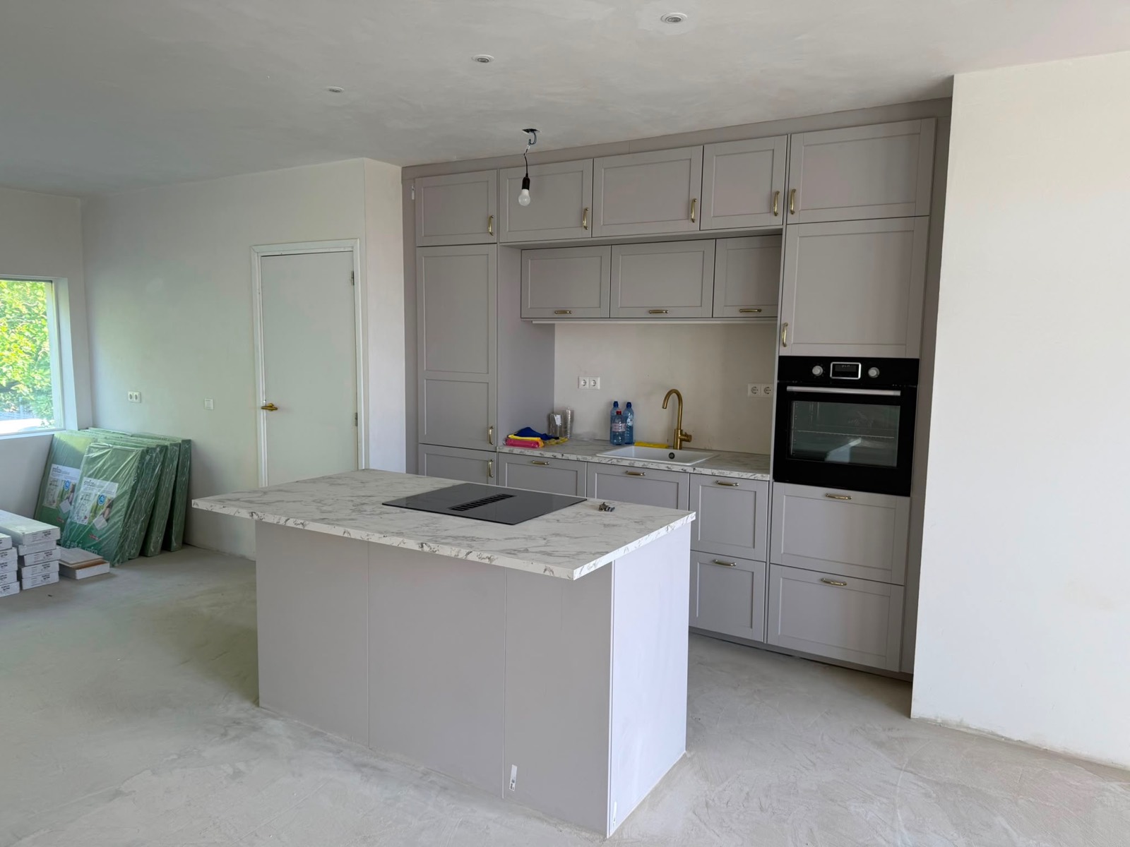 Keuken met grijze kasten, een kookeiland met marmerlook werkblad en messing details, geplaatst in de gestucte ruimte