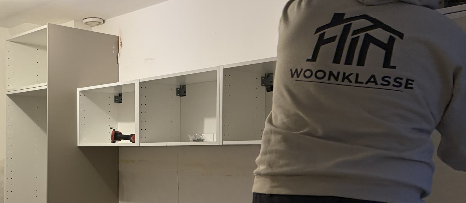 Monteur van Woonklasse hangt de bovenkasten van een keuken aan de muur