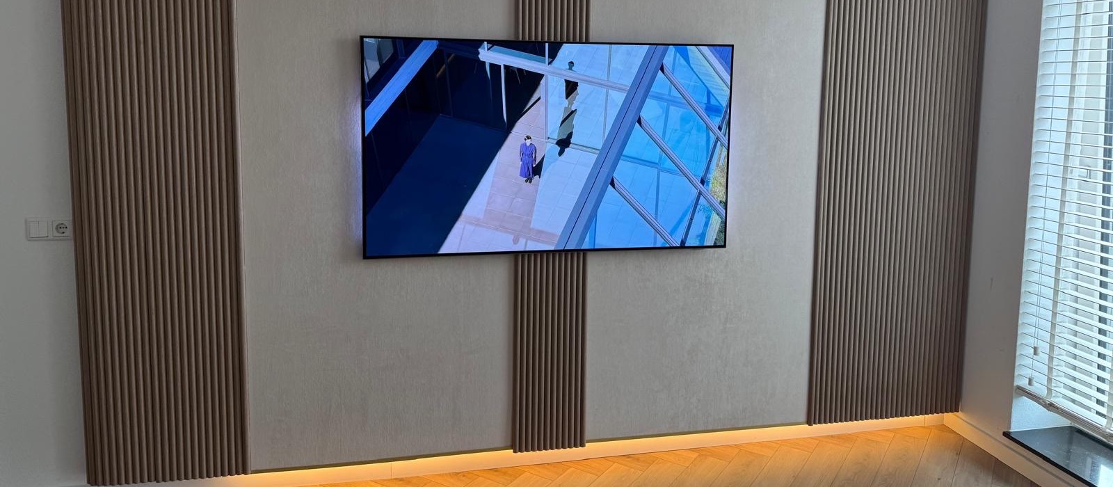 Wand met houten lattenpanelen en warme indirecte verlichting die onderlangs over de visgraatvloer valt